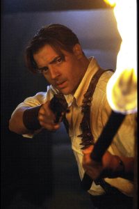 Action hero Brendan Frasier points a torch and a gun 