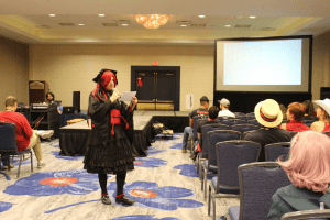 Cosplayer standing in front of a stage reading out a question for an audience
